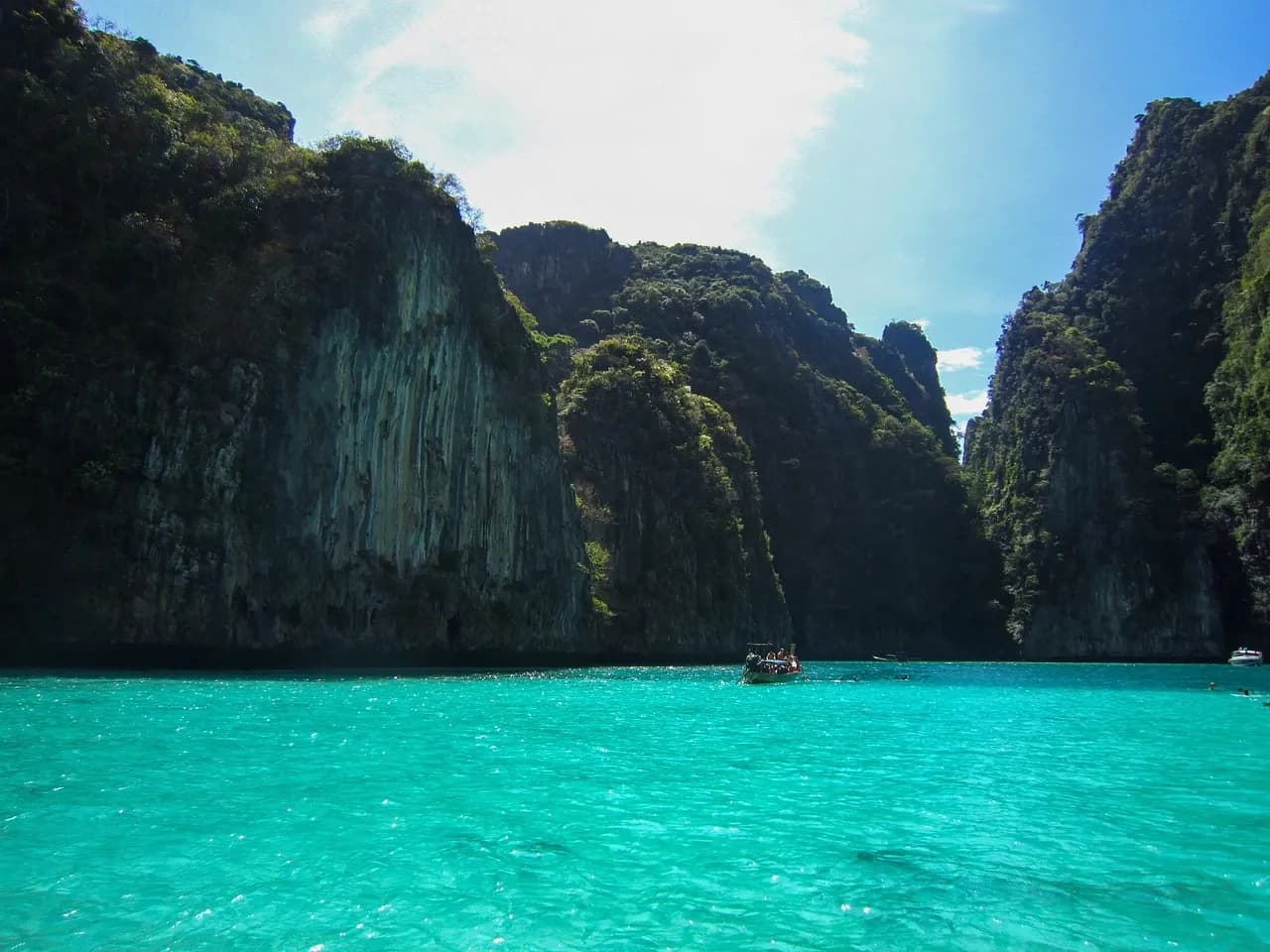 Turquoise water surrounded by tall limestone cliffs at a bay in Phi Phi Islands in Thailand with small boats on the water.